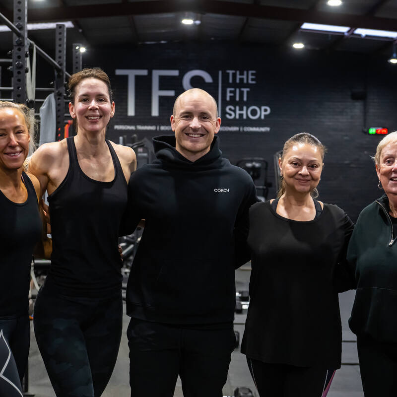 Five smiling members and coaches in front of the TFS wall