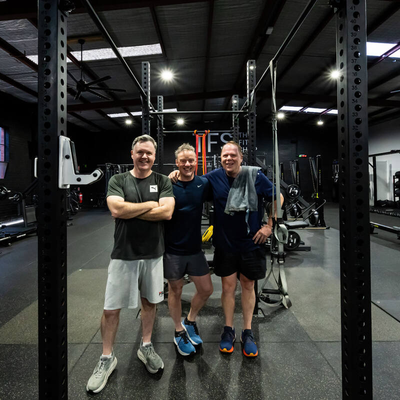 Three members standing together by the squat racks